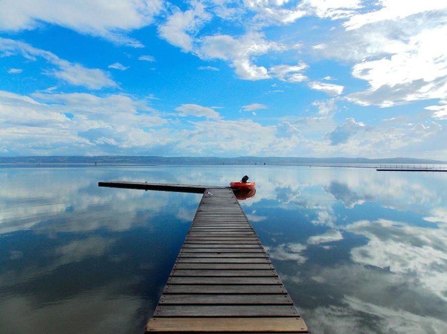 The pontoon on West Kirby Marine Lake stretching out over glassy water that mirrors the clouds, with Wales on the far shore